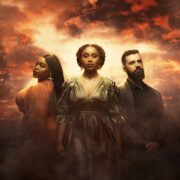 Three members of the cast stand in dramatic lighting against a cloudy, orange-lit sky: two women in ornate dresses, evoking Queen of the Fight, and a bearded man in dark clothing reminiscent of James IV.