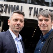 Two men stand in front of a building with a sign reading "Festival Theatre.