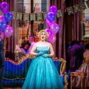 A woman in a turquoise gown sings at a lively indoor party decorated with purple balloons and a "Happy Birthday Boss" banner.