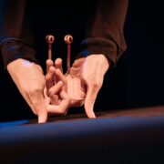 Two hands positioned upside down on a surface, with small puppet-like eyes attached to the index fingers, creating a playful character.