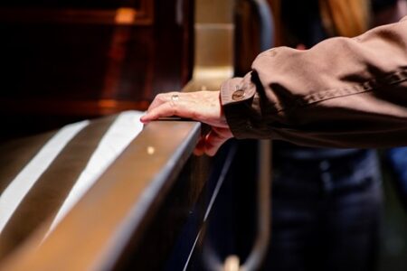 A hand resting on a banister in a theatre, adorned with a ring, against a blurred background.