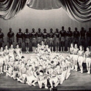 A large group of performers in uniform pose in formation on stage with curtains, promoting "The Gang Show 1960" at King's Theatre, as shown in the event poster inset.