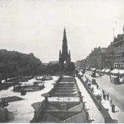 Black and white photo of a busy Princes Street with trams, pedestrians, and The Scott Monument at the center.