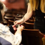 A person hands an assistive listening device to another person seated in athe theatre.