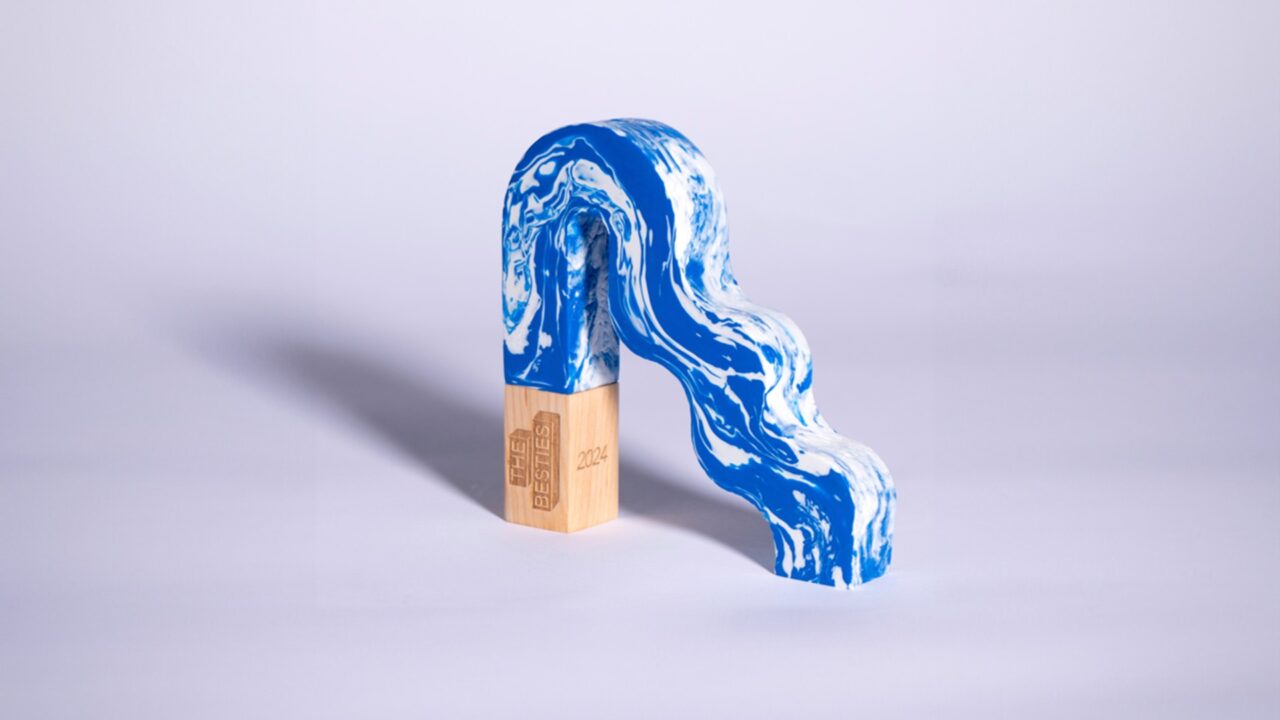 A blue and white marbled, arch-shaped object rests on a wooden rectangular block with engraved text, set against a plain light background.