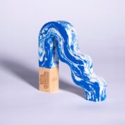 A blue and white marbled, arch-shaped object rests on a wooden rectangular block with engraved text, set against a plain light background.