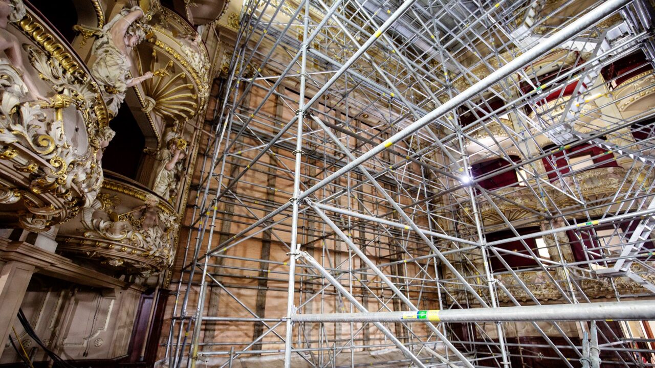 Scaffolding set up inside an ornate, historic theater with decorative balconies and detailed architectural features.