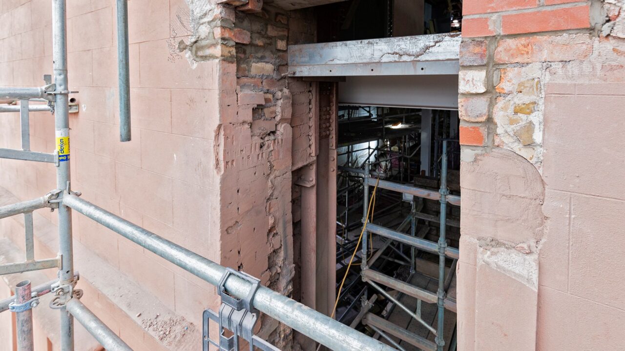 A close-up view of a partially demolished brick and stone wall, showing exposed scaffolding and interior construction materials.