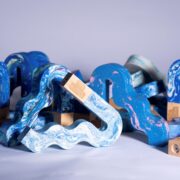 Several wavy, multicoloured objects with marbled patterns and wooden bases are arranged on a light surface against a plain background.